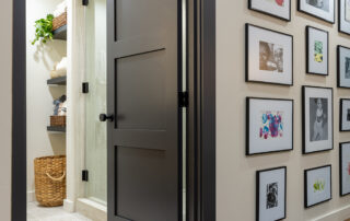A modern gray three-panel interior door partially open to a bathroom with light tile flooring, built-in shelves, and a gallery wall of framed photos in the hallway.