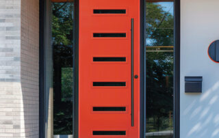 Modern home exterior featuring a bold red front door with horizontal glass inserts, black trim, and side windows